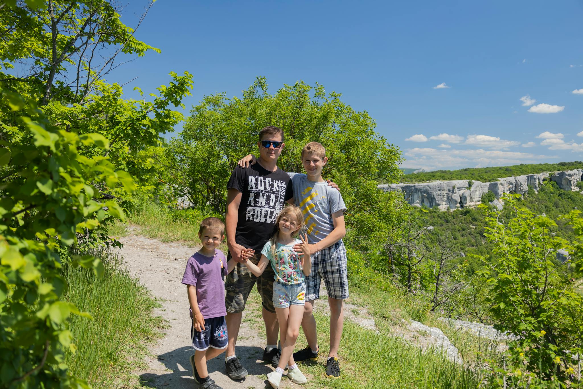 Father and children enjoying a sunny day hike with picturesque cliff backdrop.